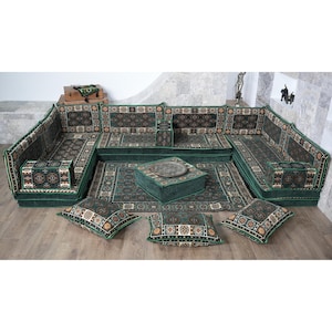 May include: A green sectional sofa with patterned cushions and a matching rug. The sofa has a low profile and is arranged in a U-shape. A square ottoman with a metal tray sits in the center, surrounded by throw pillows.
