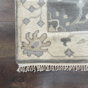 May include: A close-up of the fringe on a cream-coloured rug with a grey and beige floral pattern.