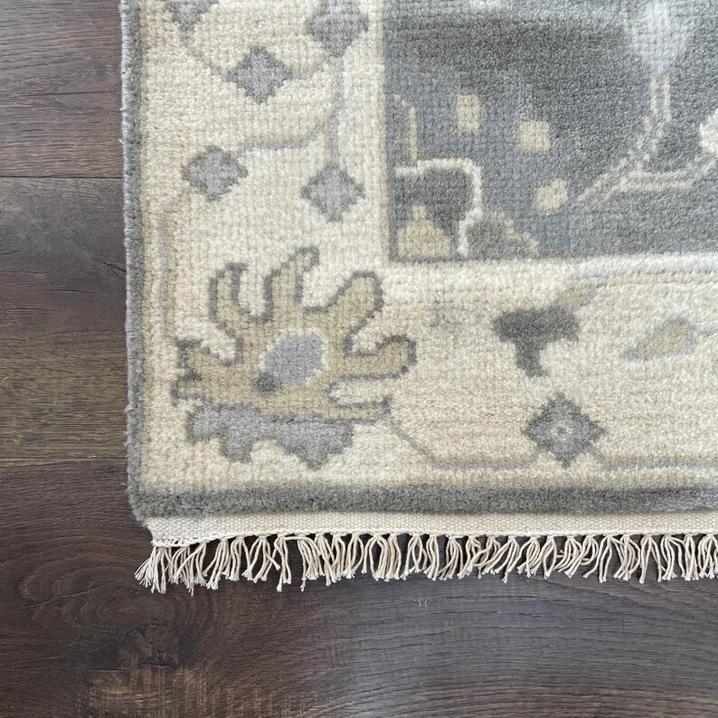 May include: A close-up of the fringe on a cream-coloured rug with a grey and beige floral pattern.