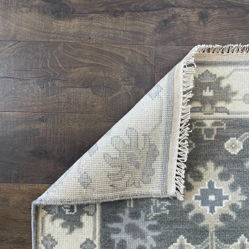 May include: A grey and white patterned rug with a fringed border. The rug is folded in half, showing the back side of the rug.