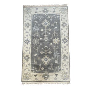 May include: A grey and beige patterned rug with a floral design. The rug has a fringed border.