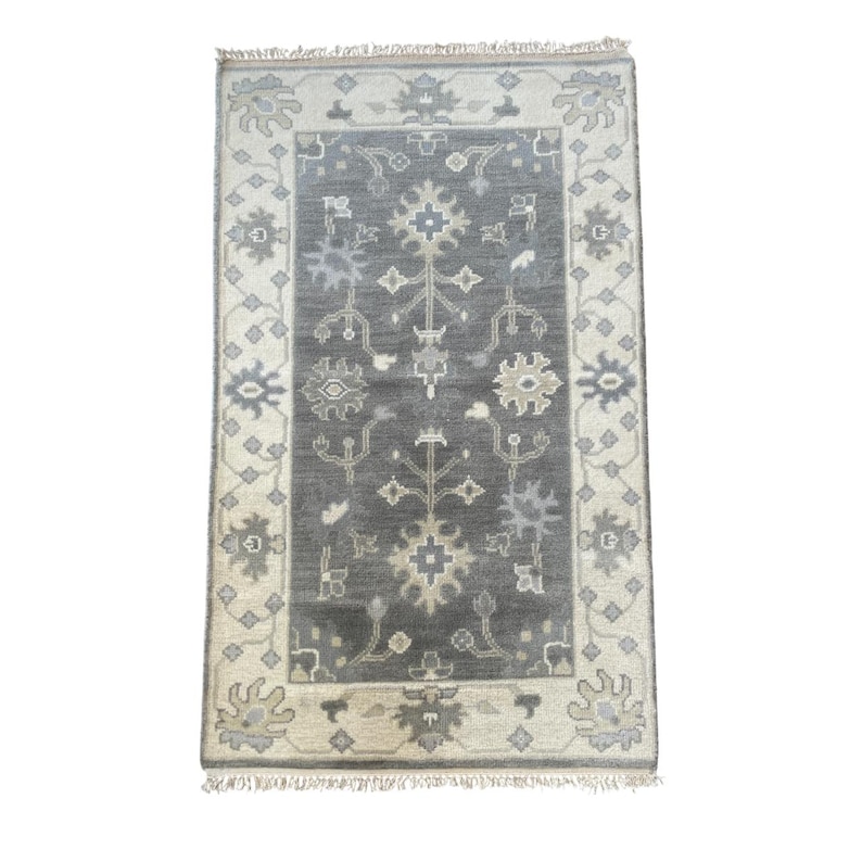 May include: A grey and beige patterned rug with a floral design. The rug has a fringed border.