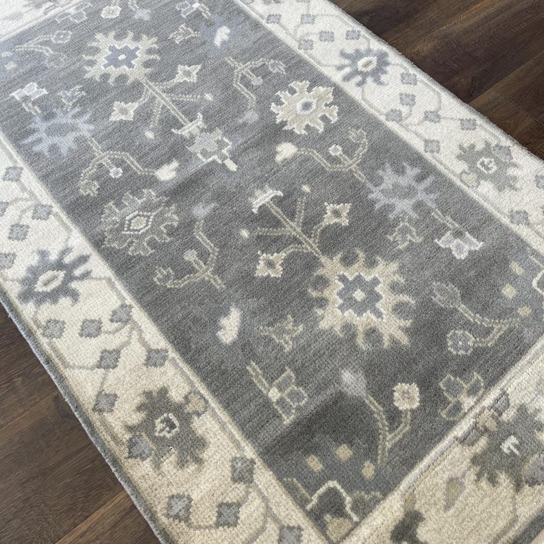 May include: A grey and cream patterned rug with a floral design. The rug has a border with a repeating pattern.