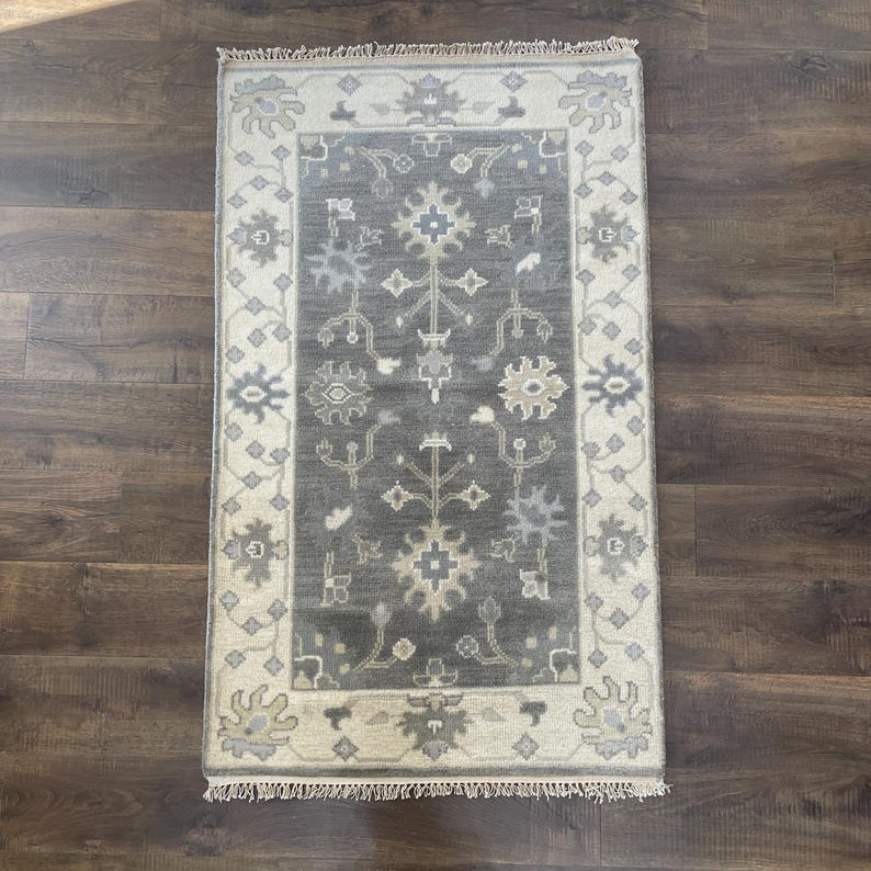 May include: A grey and cream area rug with a traditional floral pattern. The rug has a fringed border.