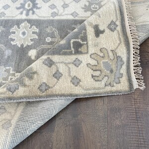 May include: A beige and grey patterned rug with a fringe border. The rug is folded in half, showing the underside of the rug.