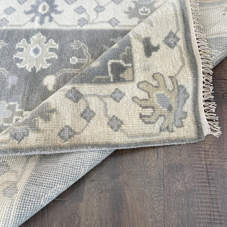 May include: A beige and grey patterned rug with a fringe border. The rug is folded in half, showing the underside of the rug.
