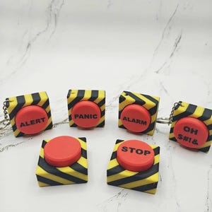 May include: Five red push button keychains with black and yellow striped designs. The buttons read "ALERT", "PANIC", "ALARM", "STOP", and "OH S#!&"