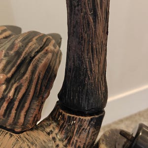May include: Close-up of a brown and black wooden-style hand with a textured surface. The hand is part of a larger decorative object.