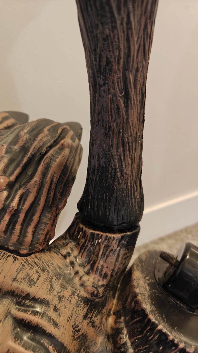 May include: Close-up of a brown and black wooden-style hand with a textured surface. The hand is part of a larger decorative object.