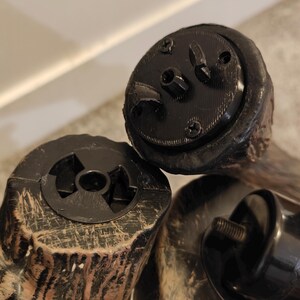May include: Close-up of two black plastic bases with a textured wood-like finish. One base has a three-pronged design, while the other has a circular design with three holes.