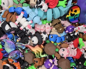 Könnte beinhalten: Eine große Sammlung von bunten, kleinen, 3D-gedruckten Figuren. Die Figuren bestehen aus verschiedenen Materialien, darunter Kunststoff, Harz und Metall. Sie zeigen eine Vielzahl von Designs, darunter Tiere, Comicfiguren und abstrakte Formen.