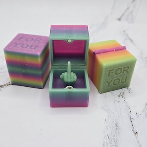 May include: Three colorful boxes with the words "For You" on them. One box is open and contains a ring with a middle finger raised.