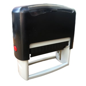 May include: A black and white self-inking stamp with a red button. The stamp has a clear plastic cover on top.