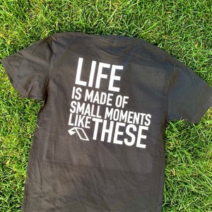May include: Black t-shirt with white text that reads "LIFE IS MADE OF SMALL MOMENTS LIKE THESE".