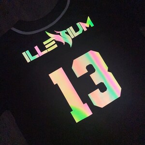 May include: Black baseball jersey with iridescent lettering and a number 13. The lettering says "ILLESIUM".