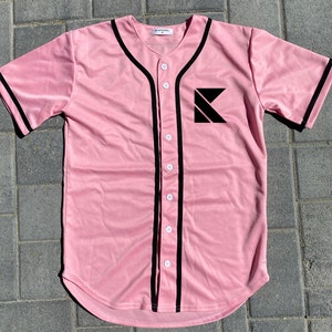 May include: A pink baseball jersey with black trim and a black letter K logo on the left chest. The jersey has a button-up front.