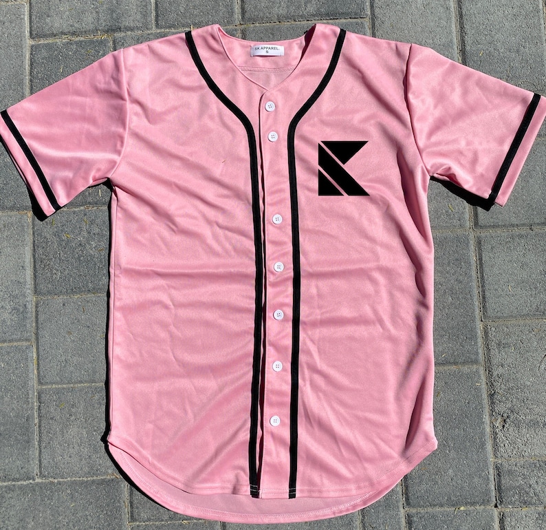 May include: A pink baseball jersey with black trim and a black letter K logo on the left chest. The jersey has a button-up front.