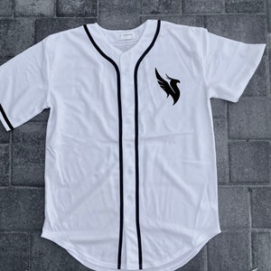 May include: White baseball jersey with black trim and a black phoenix logo on the right side. The text "LA DREAMS" is printed on the tag.