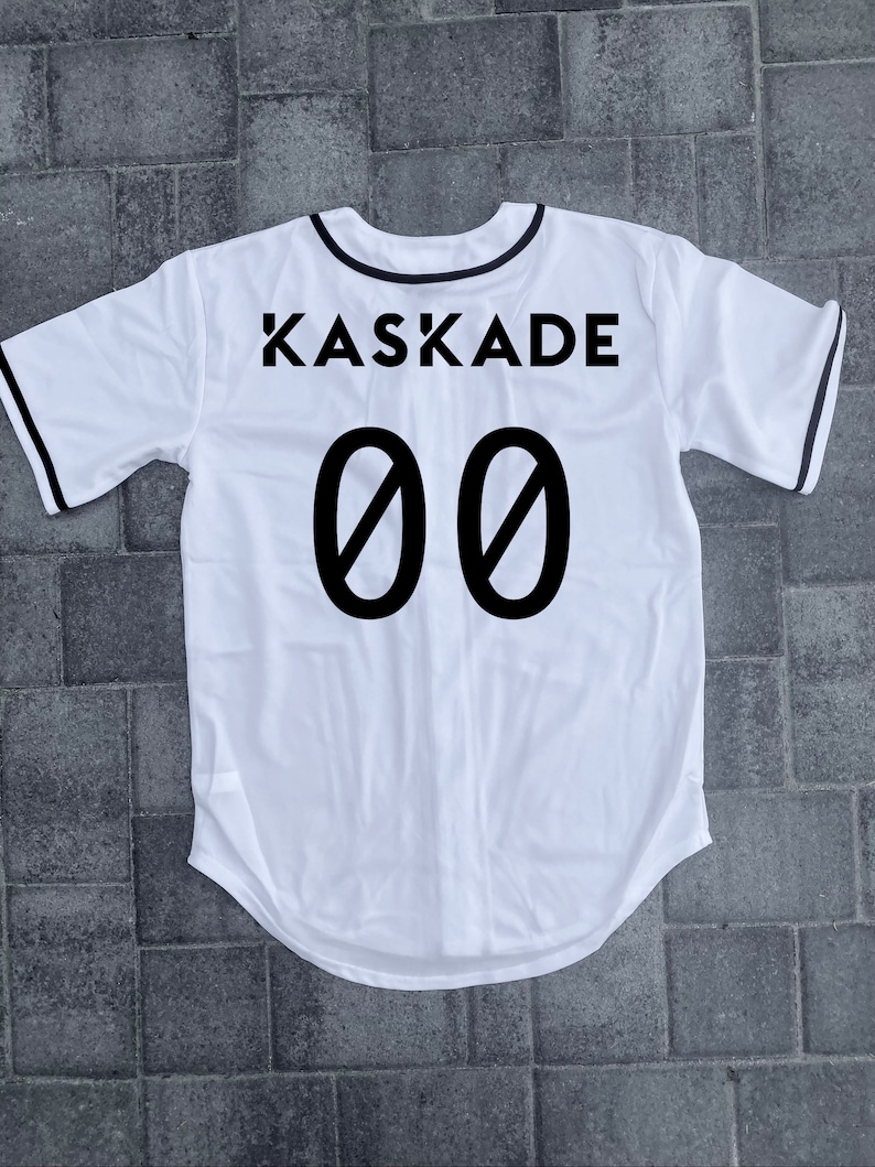 May include: White baseball jersey with black trim and the text "KASKADE 00" printed on the back.