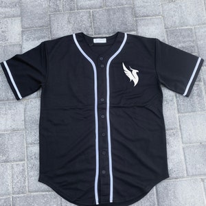 May include: Black baseball jersey with white trim and a white bird logo on the right side. The jersey has a button-up front.
