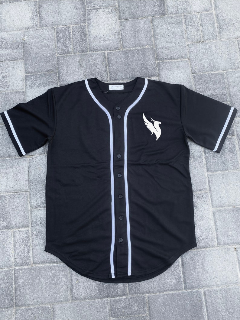 May include: Black baseball jersey with white trim and a white bird logo on the right side. The jersey has a button-up front.