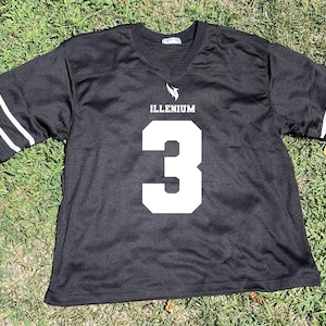 May include: Black jersey with white accents and the word "ILLENIUM" above a large white number "3". The sleeves have white stripes. The jersey is made of a breathable mesh material.