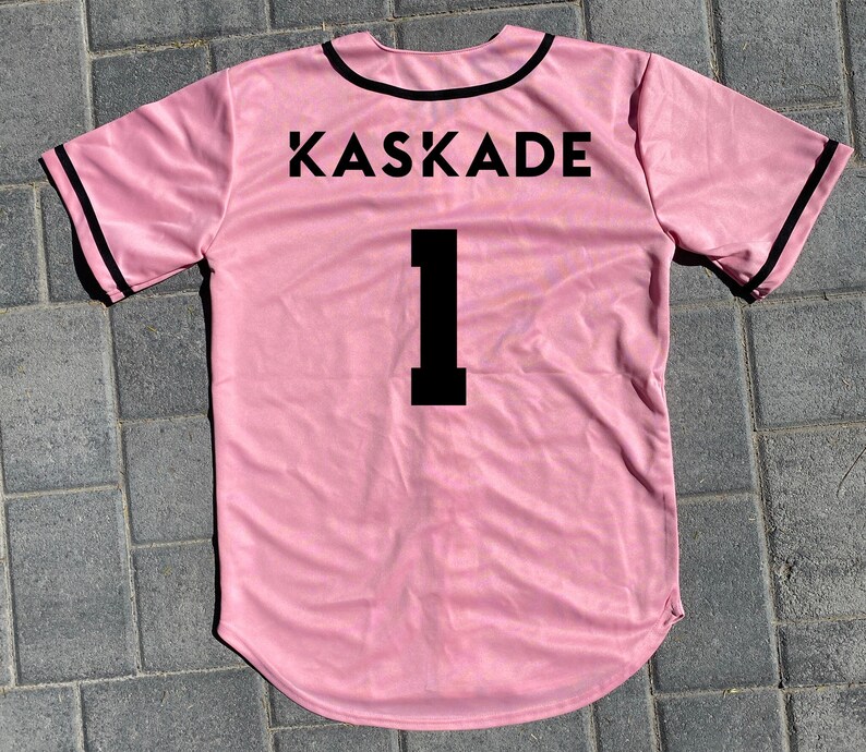 May include: Pink baseball jersey with black trim and the word "KASKADE" and the number "1" printed on the back.