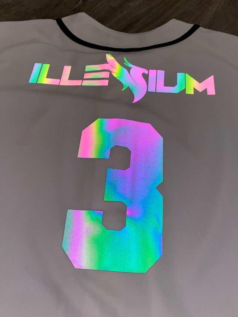 May include: A white baseball jersey with a black collar and a reflective iridescent logo that says "ILLESIUM" and the number "3" on the back.
