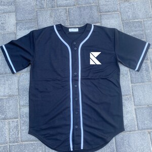 May include: Black baseball jersey with white trim and a white letter K logo on the front.