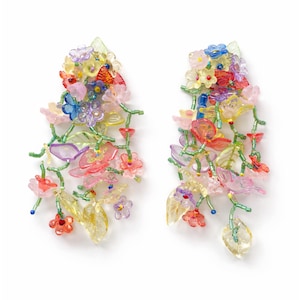 Könnte beinhalten: Ein Paar bunte Blumenohrringe. Die Ohrringe zeigen eine Kaskade aus durchscheinenden Blüten in Rosa-, Gelb-, Blau- und Lilatönen mit grünen Stielen und Blättern. Die Ohrringe sind vor einem weißen Hintergrund platziert.