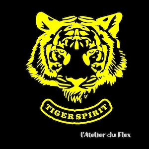 Peut inclure: Graphique noir avec une tête de tigre jaune et l'inscription "TIGER SPIRIT" dans une bannière jaune. Le visage du tigre est détaillé avec des lignes jaunes, sur fond noir. Le texte "l'Atelier du Flex" est en bas.