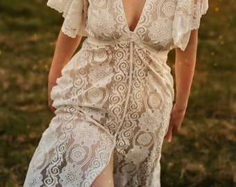 May include: A white lace maxi dress with a plunging neckline and a thigh-high slit. The dress is sheer and has a delicate floral pattern.