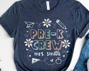 Peut inclure: T-shirt bleu marine avec l'inscription "PRE-K CREW mrs. smith" en lettres colorées et des graphiques ludiques. Le t-shirt est associé à un jean bleu et des baskets blanches, créant un thème décontracté de la rentrée scolaire.