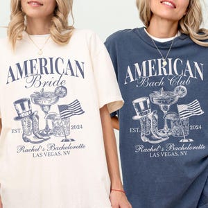 May include: Ivory and denim blue t-shirts with the text "AMERICAN Bride" and "AMERICAN Bach Club" in a vintage style. Each shirt features a graphic of a cowboy hat, boots, cocktails, and an American flag. The text "Rachel's Bachelorette Las Vegas, NV 2024" is also included.
