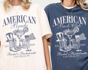Könnte beinhalten: Zwei T-Shirts, eines in Elfenbein und eines in Jeansblau, mit den Aufschriften "AMERICAN Bride" und "AMERICAN Bach Club". Jedes Shirt hat eine Grafik von Cowboyhut, Stiefeln, Cocktails und einer amerikanischen Flagge. Der Text "Rachel's Bachelorette Las Vegas, NV 2024" ist ebenfalls enthalten.