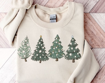 Może przedstawiać: Beżowa bluza z nadrukiem czterech choinek ozdobionych zębami. Choinki są zielone z białymi zębami i żółtymi ozdobami. Bluza ma metkę Gildan.