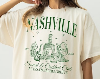 以下が含まれることがあります： 「Nashville Social & Cocktail Club Alyssa's Bachelorette」と緑色のグラフィックデザインが施された白いオーバーサイズTシャツ。ギター、羽根、ボトル、グラス、カウボーイハットがデザインされています。