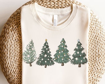 Könnte beinhalten: Ein weißes T-Shirt mit einem Design aus fünf grünen Weihnachtsbäumen, die mit weißen Zähnen als Ornamenten verziert sind. Die Bäume sind in einer Reihe über die Mitte des Shirts angeordnet. Das Shirt ist gefaltet und auf einer gewebten Matte ausgestellt.