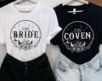 May include: Two t-shirts, one white and one black, each with a circular graphic. The white shirt says "THE BRIDE" and the black shirt says "THE COVEN". Both designs include stars, crystals, and floral elements.