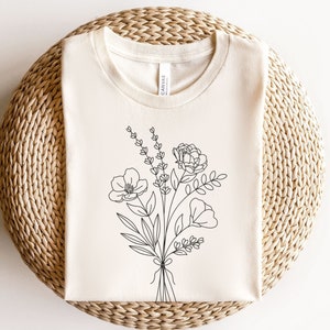 以下が含まれることがあります： 白いTシャツに、黒い線で描かれた花束のイラスト。花束には、バラ、ポピー、ラベンダーが含まれています。