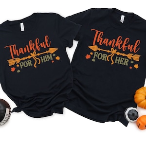 May include: Two black t-shirts with a Thanksgiving theme. The left shirt says "Thankful for Him" with an arrow and fall leaves. The right shirt says "Thankful for Her" with an arrow and fall leaves.