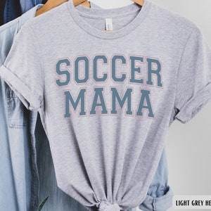 May include: Light grey heather t-shirt with the text "SOCCER MAMA" in blue with a pink outline.