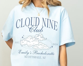Puede incluir: Camiseta azul claro con el texto "Cloud Nine Club" y un gráfico de nubes con estrellas. El texto "Est. 2024" y "Emily's Bachelorette Scottsdale, AZ" también está impreso en la camiseta.