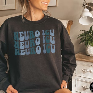 Pode incluir: Camisola de moletom preta com um gr&aacute;fico de estilo retr&ocirc; que diz "Neuro ICU" repetido tr&ecirc;s vezes em azul e turquesa.