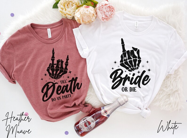 Puede incluir: Dos camisetas con una mano de esqueleto haciendo el dedo medio. La camiseta de la izquierda es de color malva jaspeado y dice "Till Death Do Us Party". La camiseta de la derecha es blanca y dice "Bride or Die".