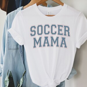 May include: White t-shirt with blue and red text that says "Soccer Mama".
