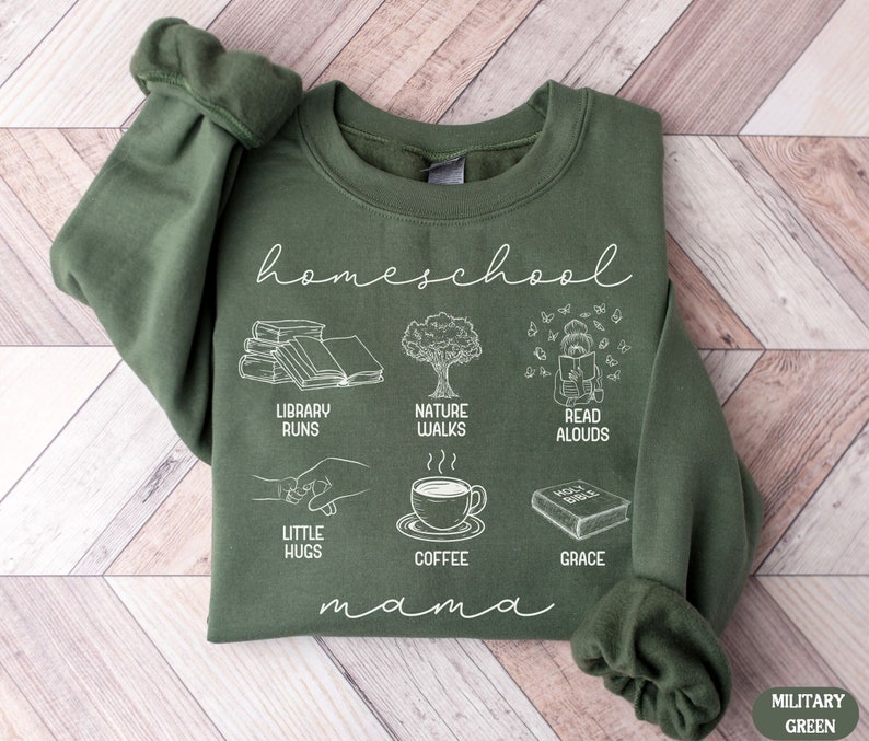 Puede incluir: Una sudadera verde con el texto "homeschool mama" e ilustraciones de libros, un &aacute;rbol, un ni&ntilde;o leyendo, manos que se toman de la mano, una taza de caf&eacute; y un libro con el texto "Holy Bible". Las ilustraciones son blancas y el texto es blanco.