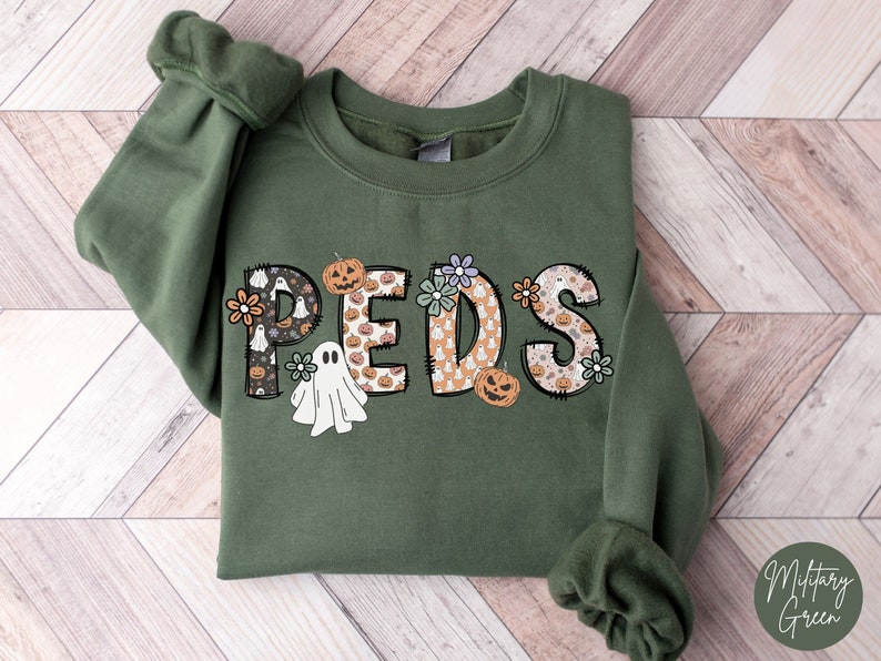 May include: A military green sweatshirt with the word "PEDS" in a decorative font. The letters are filled with Halloween-themed patterns, including ghosts, pumpkins, and flowers. The sweatshirt has long sleeves and a crew neck.