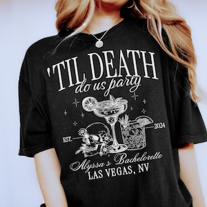 May include: Black t-shirt with white text that reads "'Til Death Do Us Party" with a skull and crossbones, two cocktails, and the text "Est. 2024 Alyssa's Bachelorette Las Vegas, NV".
