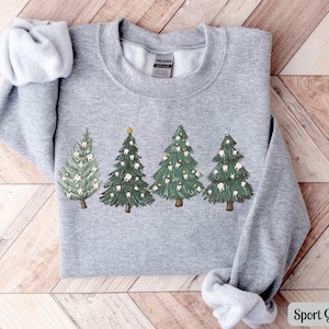 K&ouml;nnte beinhalten: Ein graues Sweatshirt mit einem Weihnachtsbaum-Design, das Z&auml;hne als Schmuck verwendet. Die B&auml;ume sind gr&uuml;n mit wei&szlig;en Z&auml;hnen und gelben Sternen. Das Sweatshirt ist in Sportgrau gehalten.